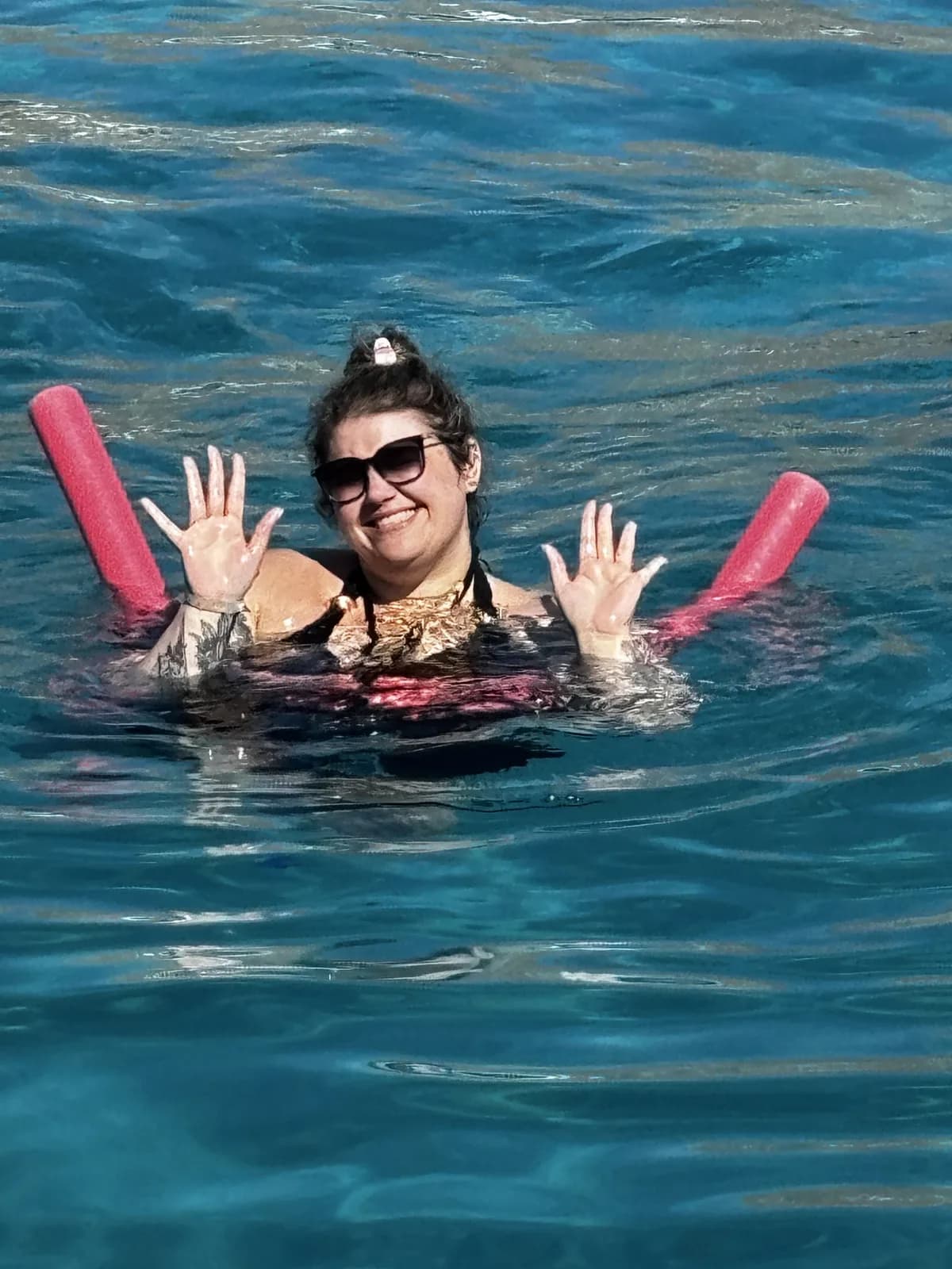 Alex floating in the pool with pink noodles